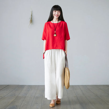 Woman smiling wearing red asymmetrical hem loose top and white pants