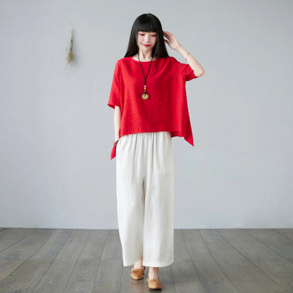 Front view of woman wearing red asymmetrical short sleeve top with white wide leg pants