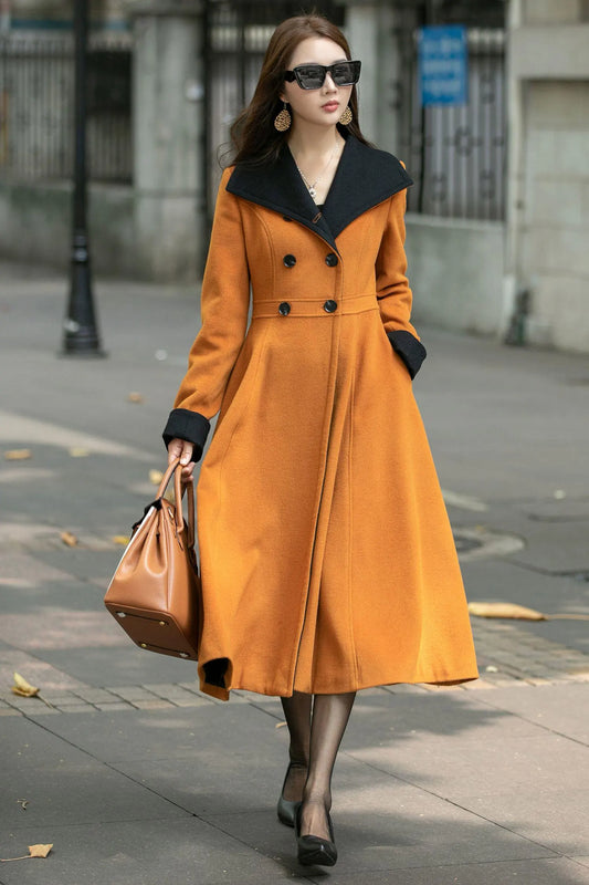 May include: A mustard yellow double-breasted wool coat with a black collar. The coat has long sleeves, a belted waist, and a flared hem.  The coat is midi length and features a classic, elegant design.  It is shown on a mannequin against a city street ba