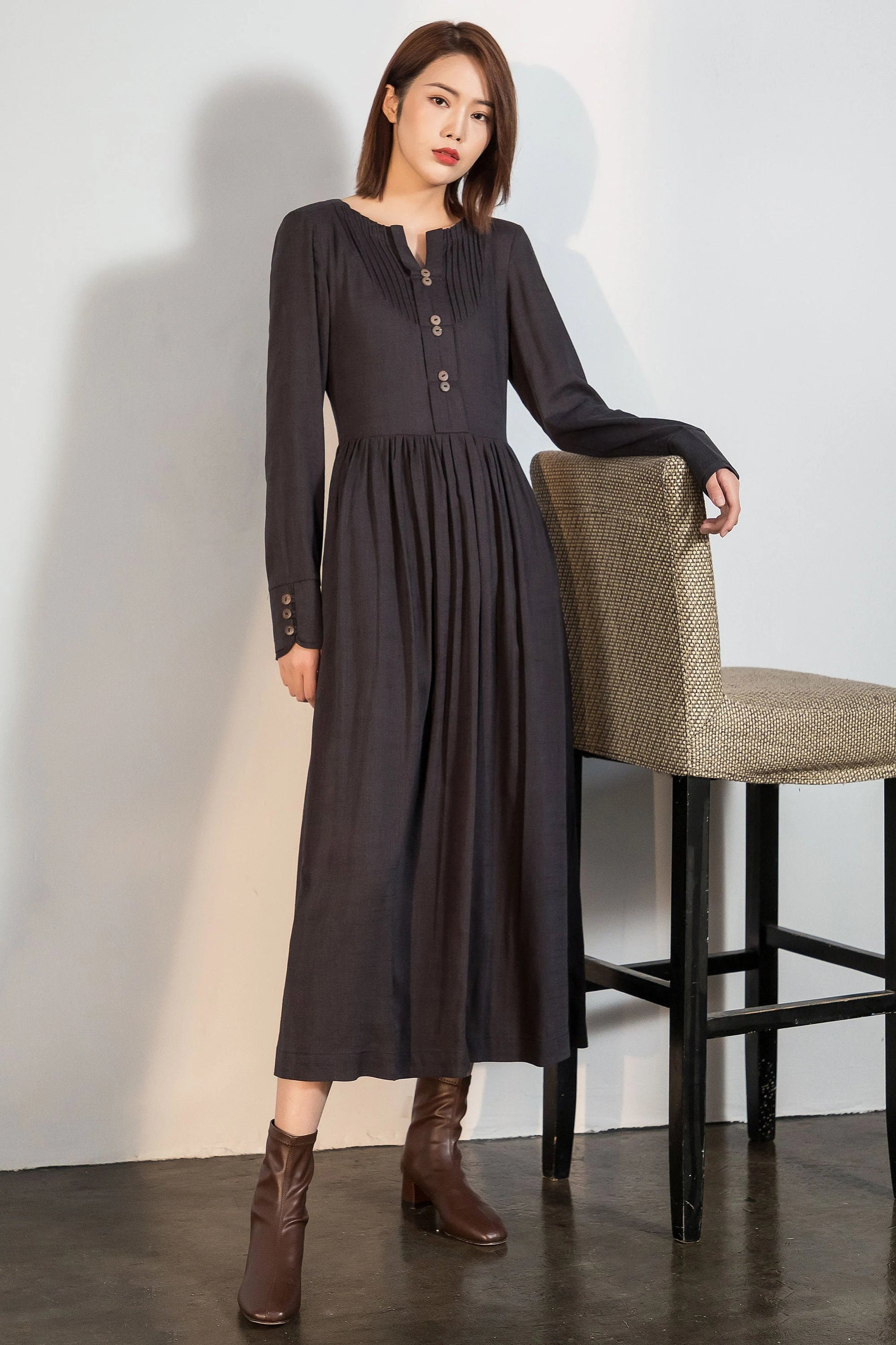 May include: A long-sleeved, dark gray dress with a button-up front and a gathered skirt. The dress has a v-neck and is worn with brown ankle boots.