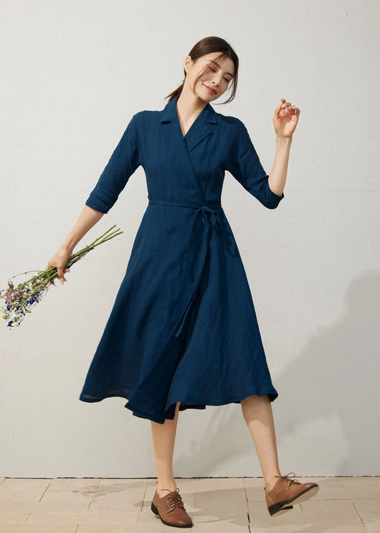 Model wearing navy blue linen wrap dress with half sleeves and belted waist holding flowers