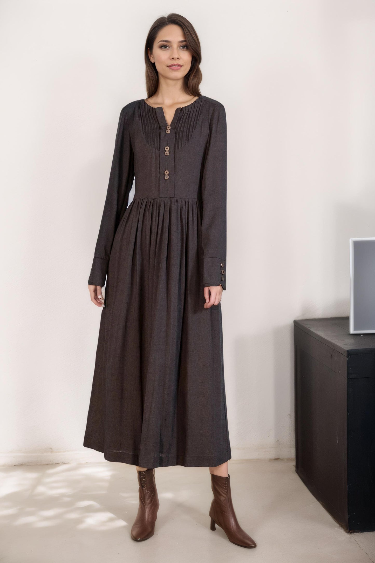 May include: A long-sleeved, dark brown dress with a button-up front and a gathered skirt. The dress has a v-neckline and a fitted bodice. The model is wearing brown ankle boots.