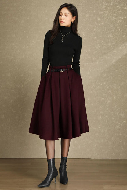 May include: A woman wearing a black turtleneck sweater, a burgundy pleated skirt, and black ankle boots. The skirt is cinched at the waist with a black belt. The outfit is suitable for fall or winter wear.