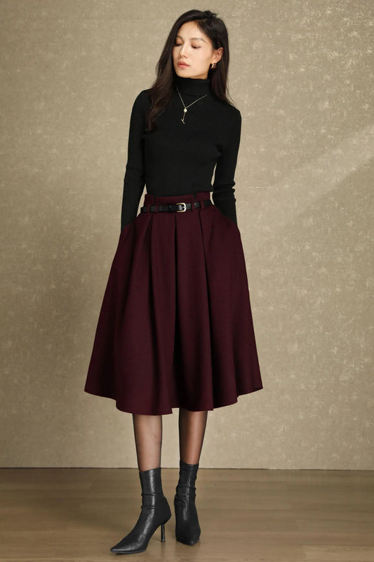 May include: A woman wearing a black turtleneck sweater, a burgundy pleated skirt, and black ankle boots. The skirt is cinched at the waist with a black belt. The outfit is suitable for fall or winter wear.